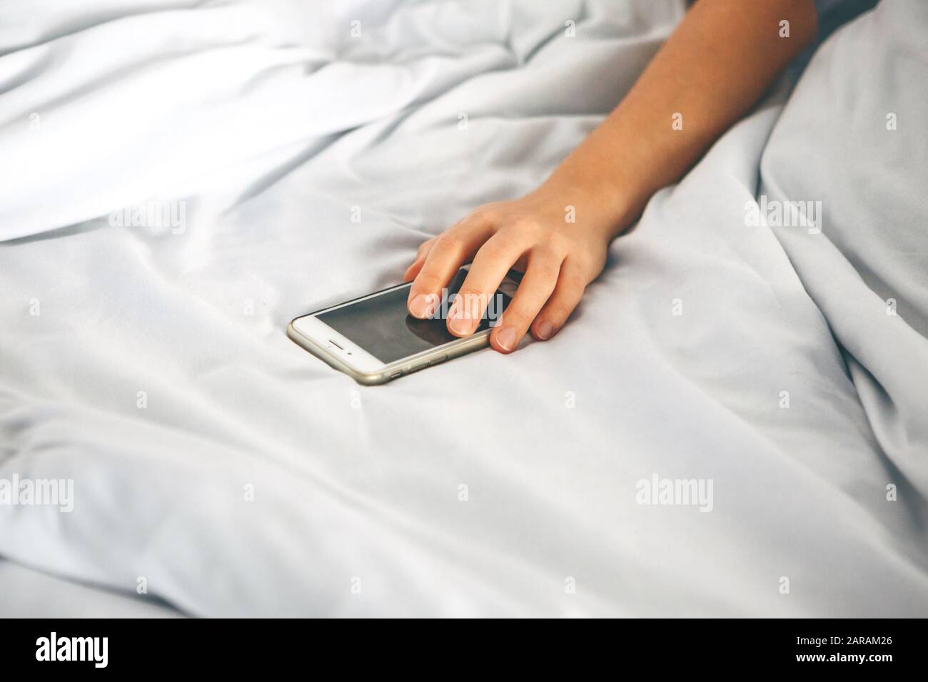 La main de gros plan maintient le téléphone dans le lit. La fille s'est endormie avec un téléphone dans sa main et elle est accro. Ou une personne atteint pour qu'un téléphone mobile désactive l'alarme. Banque D'Images