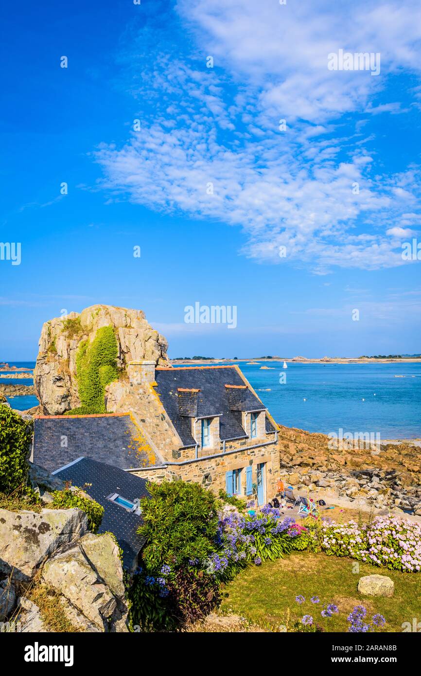 Maison en granit breton avec toit en ardoise dans le petit port de Pors Hir en Bretagne, construite sur le bord de mer à côté d'un bloc, par une journée d'été ensoleillée. Banque D'Images