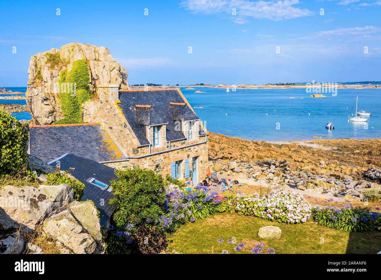 Maison en granit breton avec toit en ardoise dans le petit port de Pors Hir en Bretagne, construite sur le bord de mer à côté d'un bloc, par une journée d'été ensoleillée. Banque D'Images