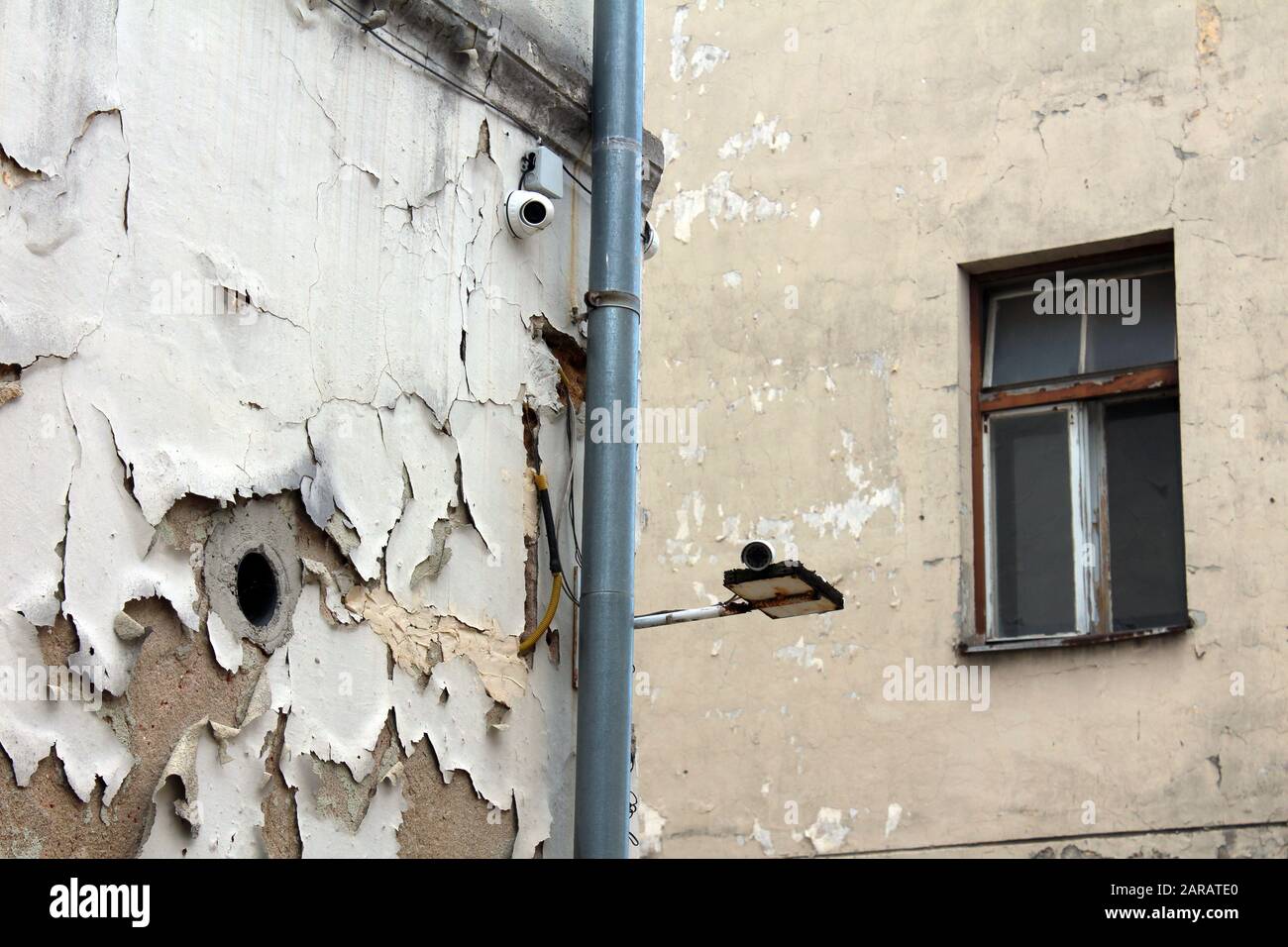 Nouvelles caméras de vidéosurveillance en circuit fermé montées à l'angle de l'ancien bâtiment abandonné avec une façade fissurée délabrée à côté du nouveau tuyau de gouttière dans l'ancien Banque D'Images