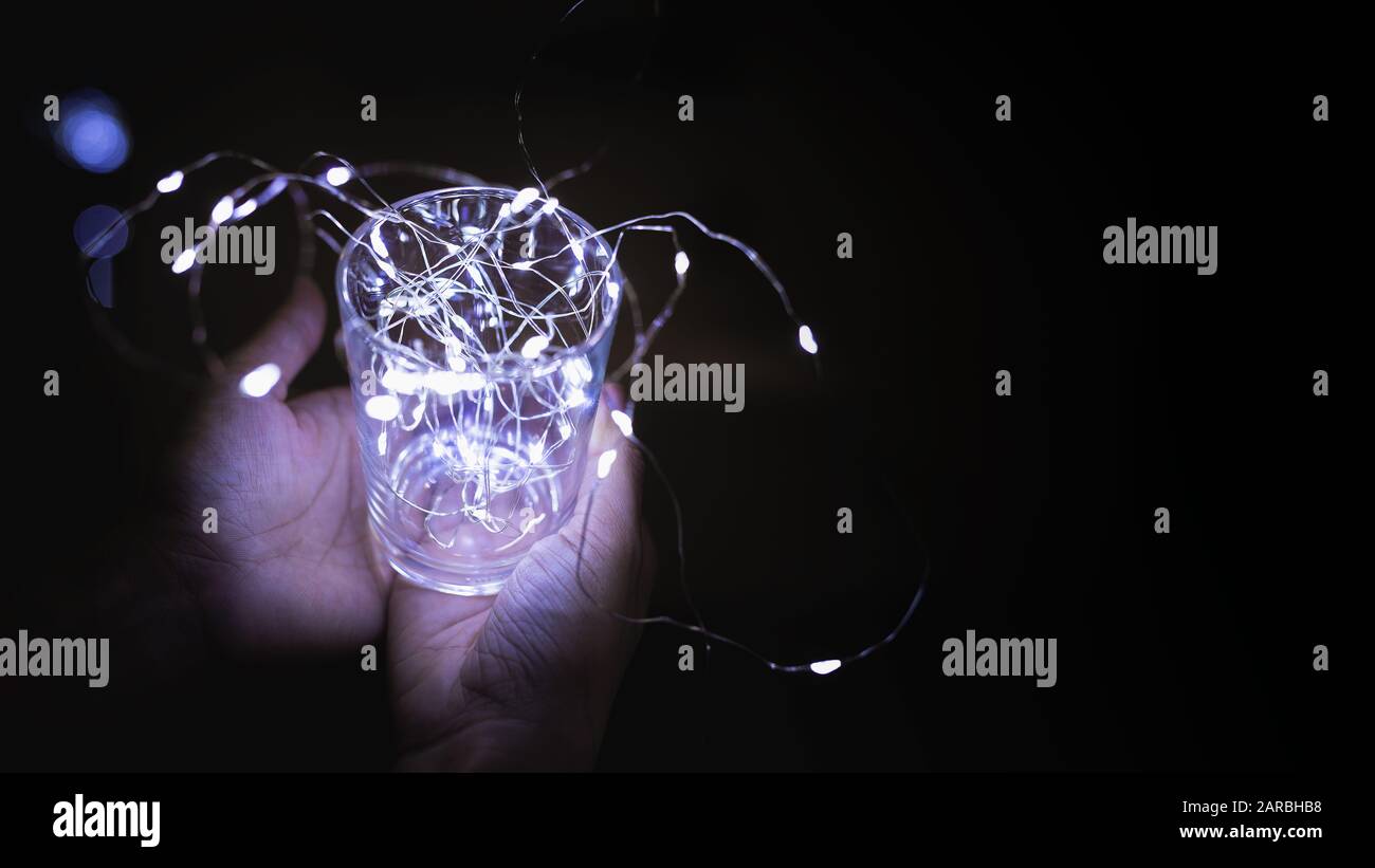 Verre de minuscules lumières à la décoration blanche sur la main de la femme avec fond sombre. Banque D'Images