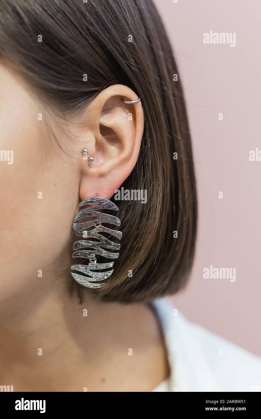 boucles d'oreilles stylées et tendance en argent sur l'oreille de la fille avec coupe bob. Fond rose pastel. Banque D'Images