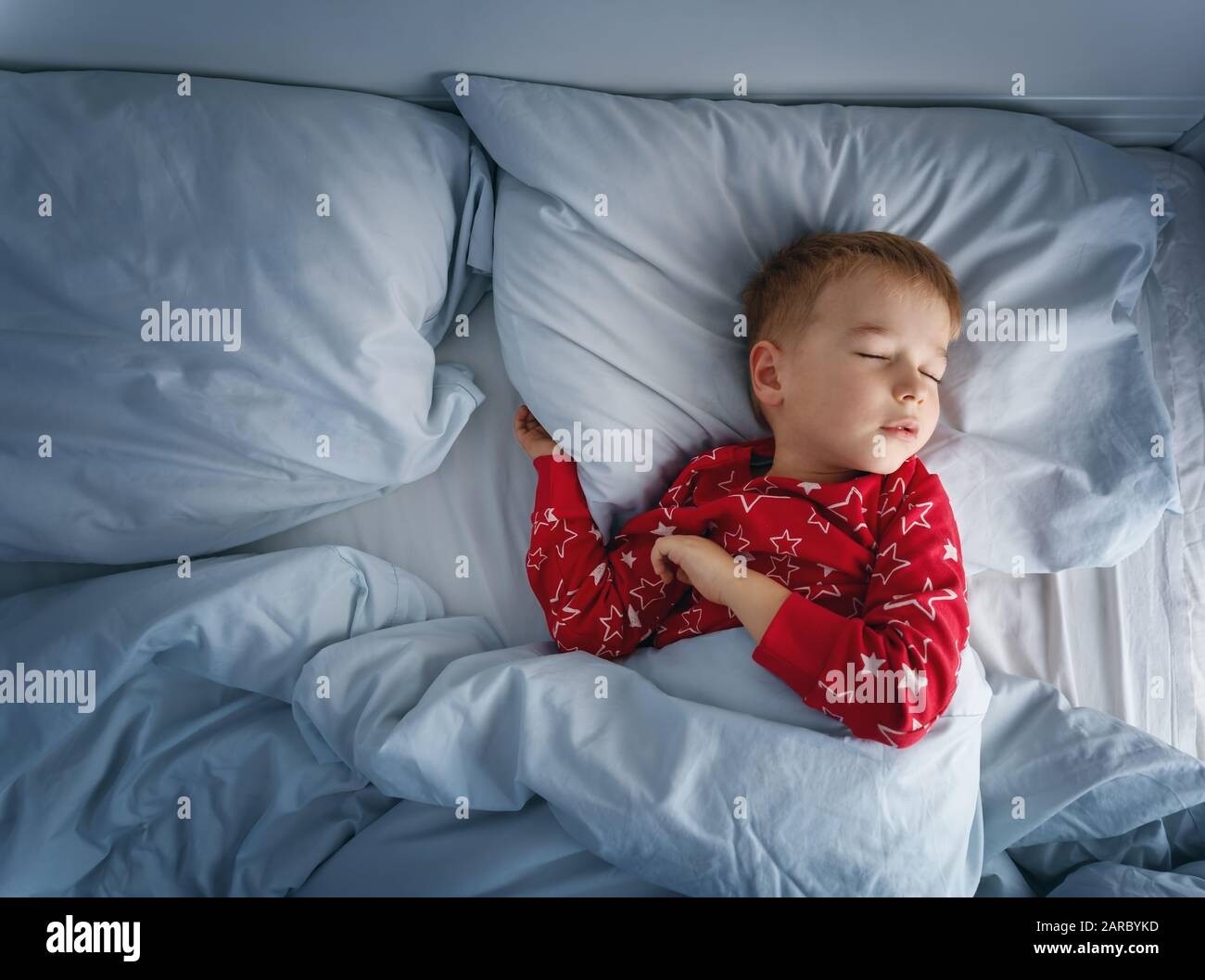 Un garçon endormi allongé dans le lit avec des couvre-lits bleus. Enfant fatigué dans la chambre Banque D'Images