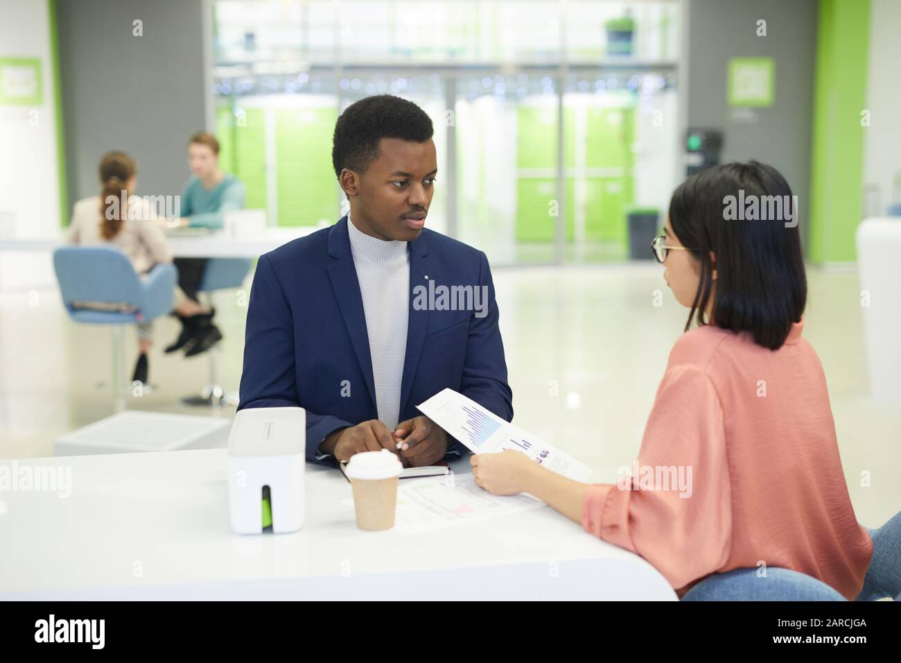 Portrait de jeunes hommes d'affaires africains discutant de documents de données avec une collègue féminine en étant assis à la table pendant la pause déjeuner au bureau Banque D'Images