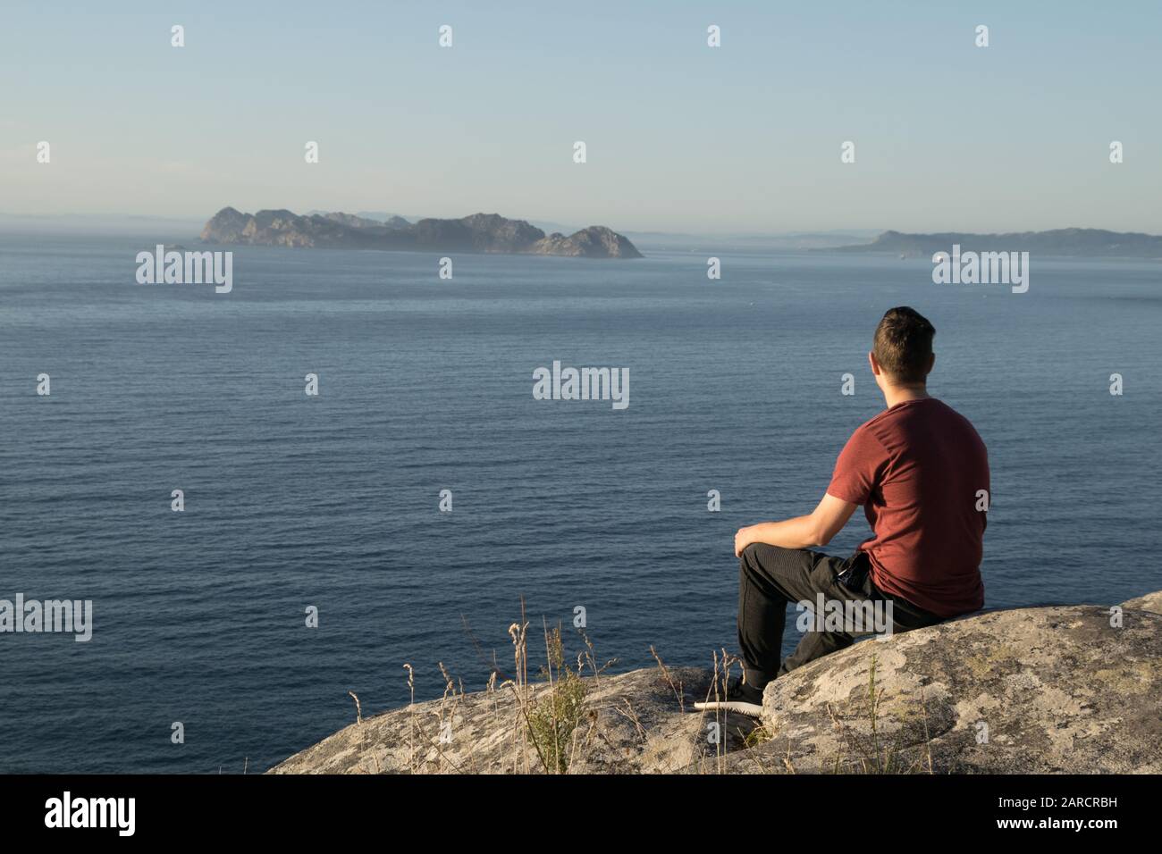 jeune garçon assis sur les rochers regardant l'horizon Banque D'Images