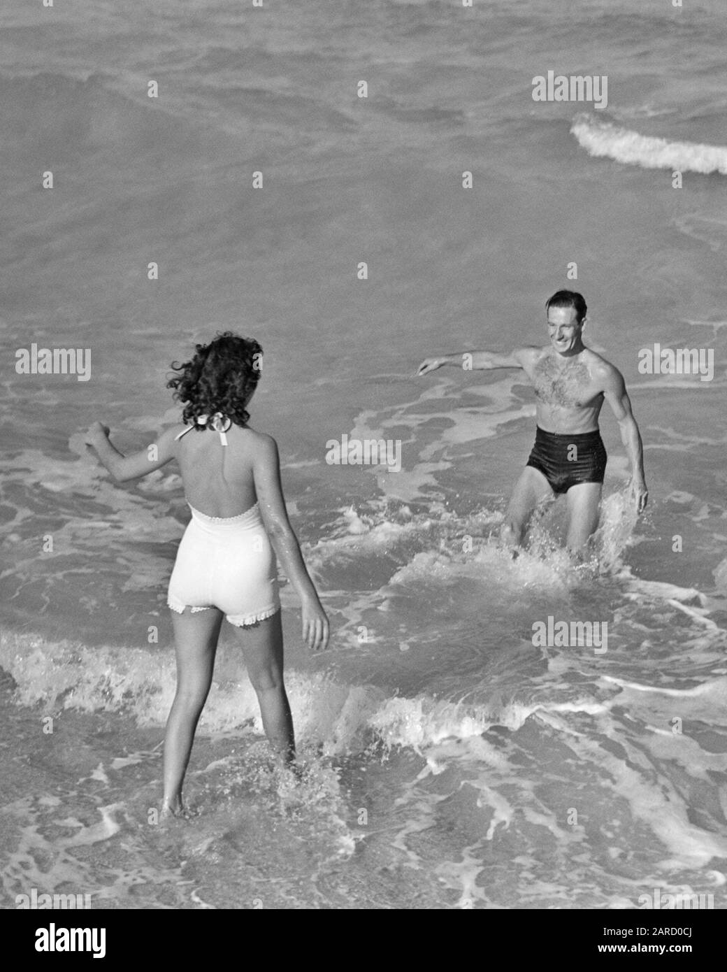 ANNÉES 1930 ANNÉES 1940 COUPLE DE VACANCES PORTANT DES COSTUMES DE BAIN  JOUANT DANS LE SURF À BEACH FEMME COURIR VERS SOURIRE HOMME FLORIDE USA -  B7126 HAR001 HARS 1 FITNESS SILLY