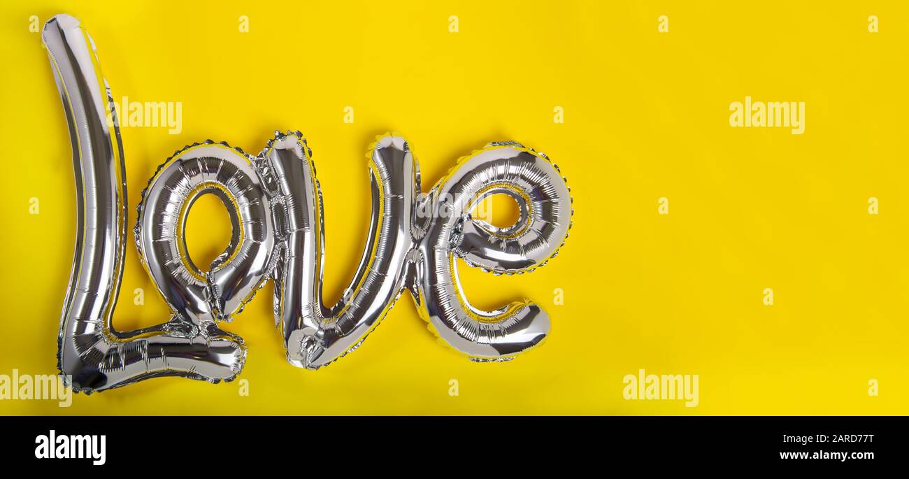 Ballons en feuille d'argent sous la forme d'un mot Amour. Bonne Saint Valentin. Concept de festival d'amour. Les ballons rendent les gens heureux. Fond jaune vif Banque D'Images