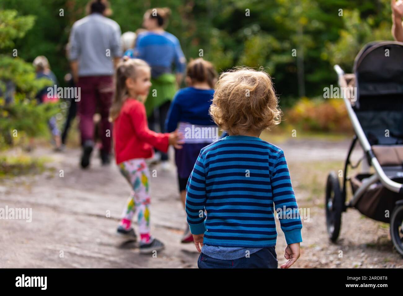 Vue Arriere Du Bebe Portant Un Pull Raye Bleu Tout En Marchant Contre Les Sœurs Et Les Parents Avec Des Arbres En Arriere Plan Au Parc Pendant La Journee Ensoleillee Photo Stock