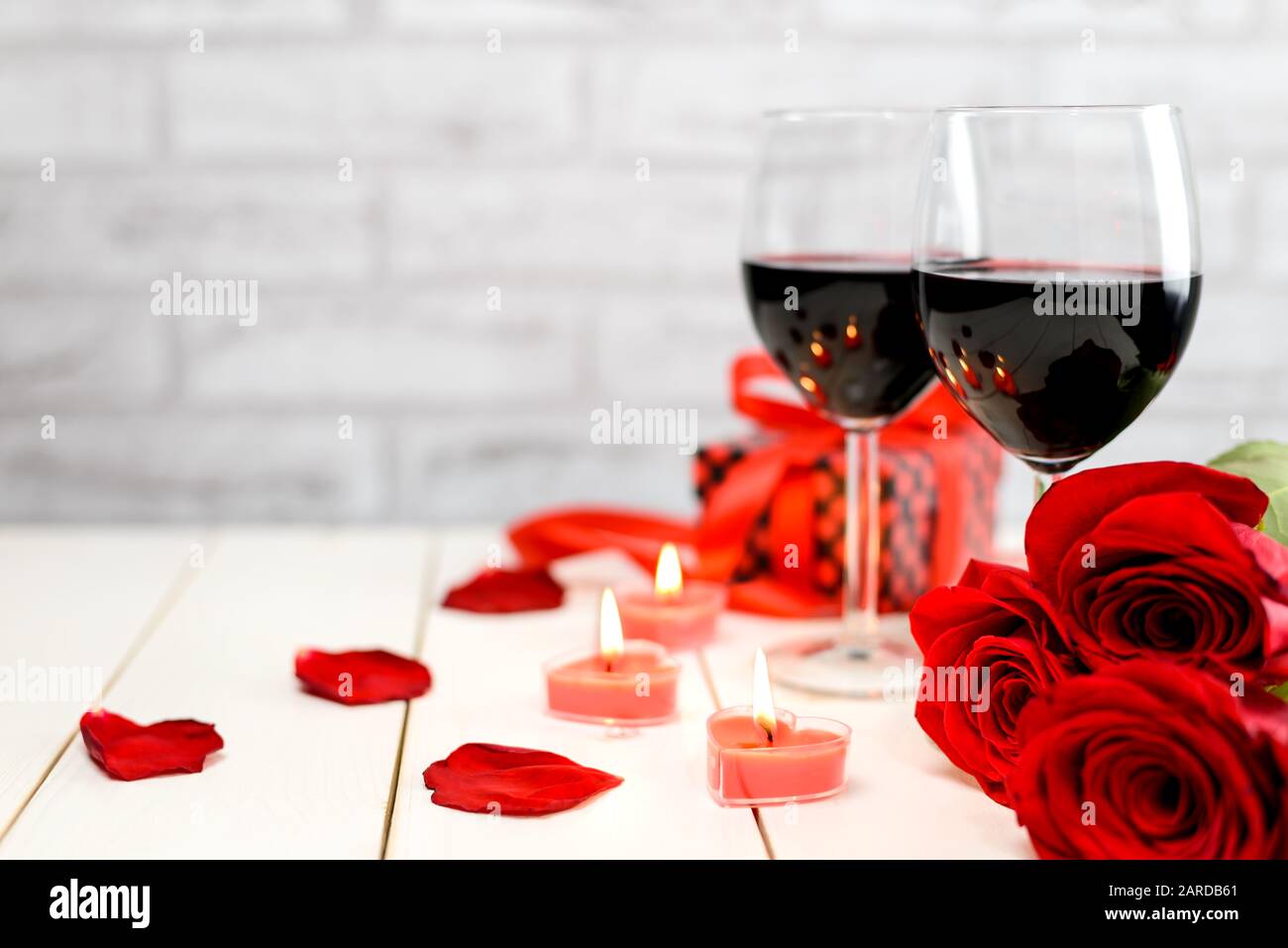 Concept Saint Valentin. Deux verres de vin, roses rouges, boîte cadeau, pétales et bougies brûlantes sur une table en bois blanc avec espace pour le texte. Sélectionnez Banque D'Images