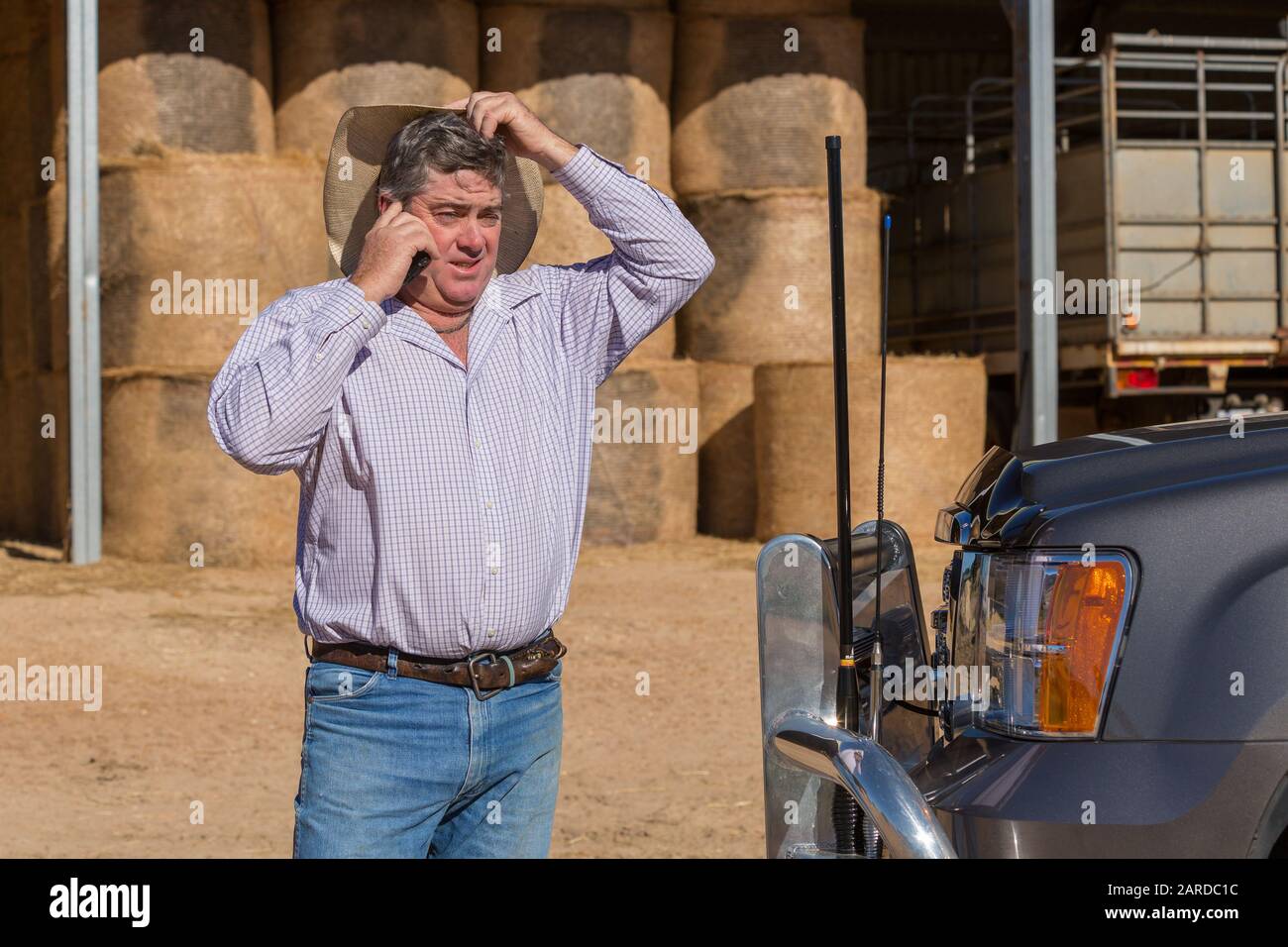 Agriculteur sur le téléphone cellulaire près du camion avec des antennes regardant confus et rayant sa tête Banque D'Images