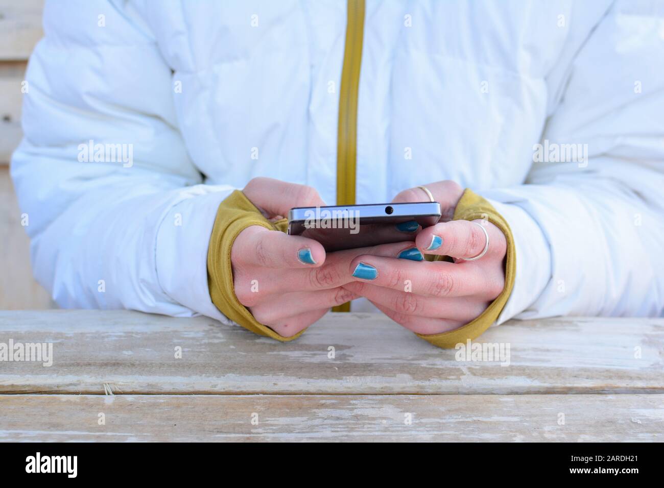 Téléphone portable utilisé par la jeune fille dans un costume de ski blanc  au-dessus de la table en bois blanc, grunge; une courte pause de l'activité  de ski et de la communication