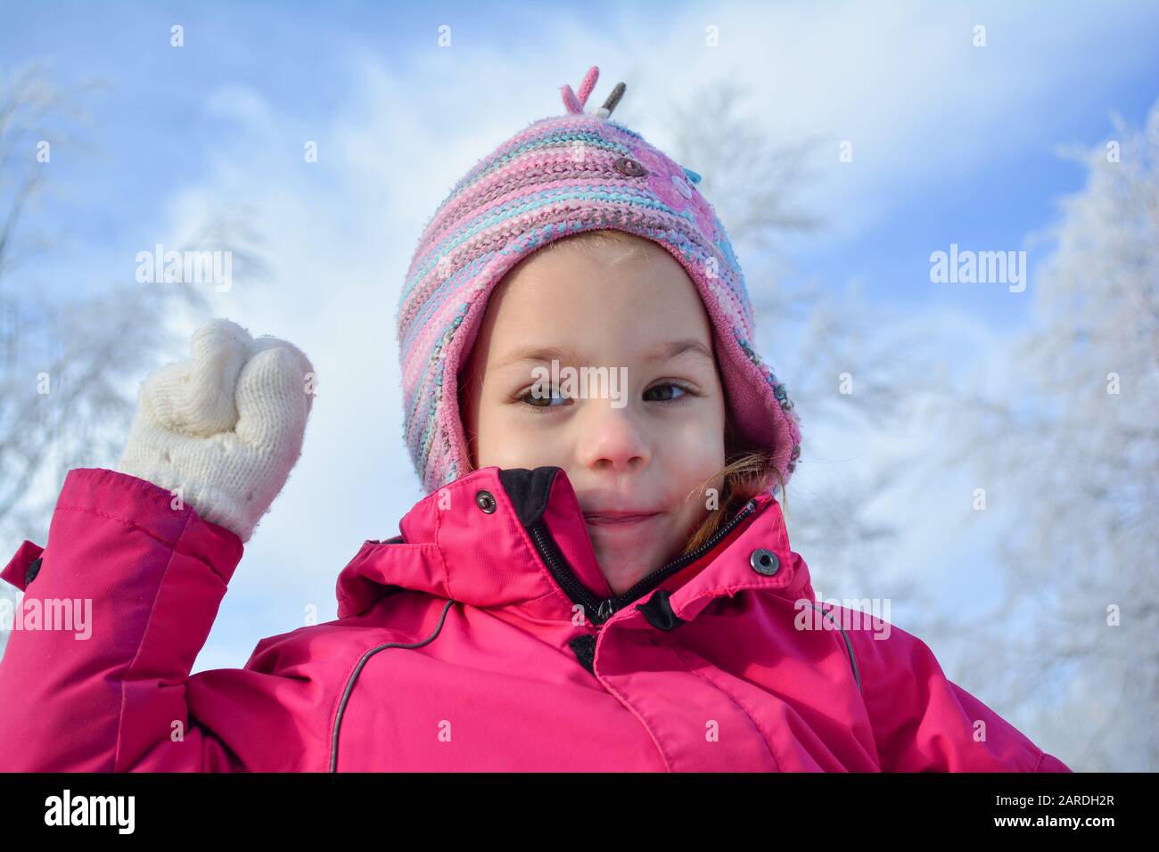 Portrait de la jeune fille en vêtements d'hiver et chapeau de laine coloré, prêt à jeter le boule de neige, contre le ciel bleu et les arbres congelés blancs bokeh Banque D'Images