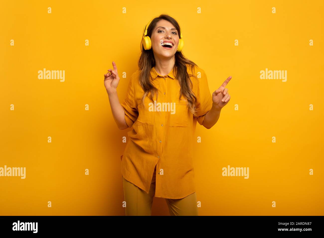 Fille avec casque jaune écoute de la musique et des danses et énergique expression émotionnelle. Banque D'Images