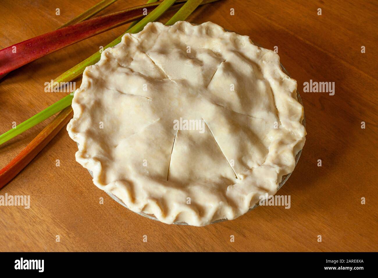 Pie de rhubarbe non cuite avec tiges de rhubarbe sur fond de bois. Banque D'Images