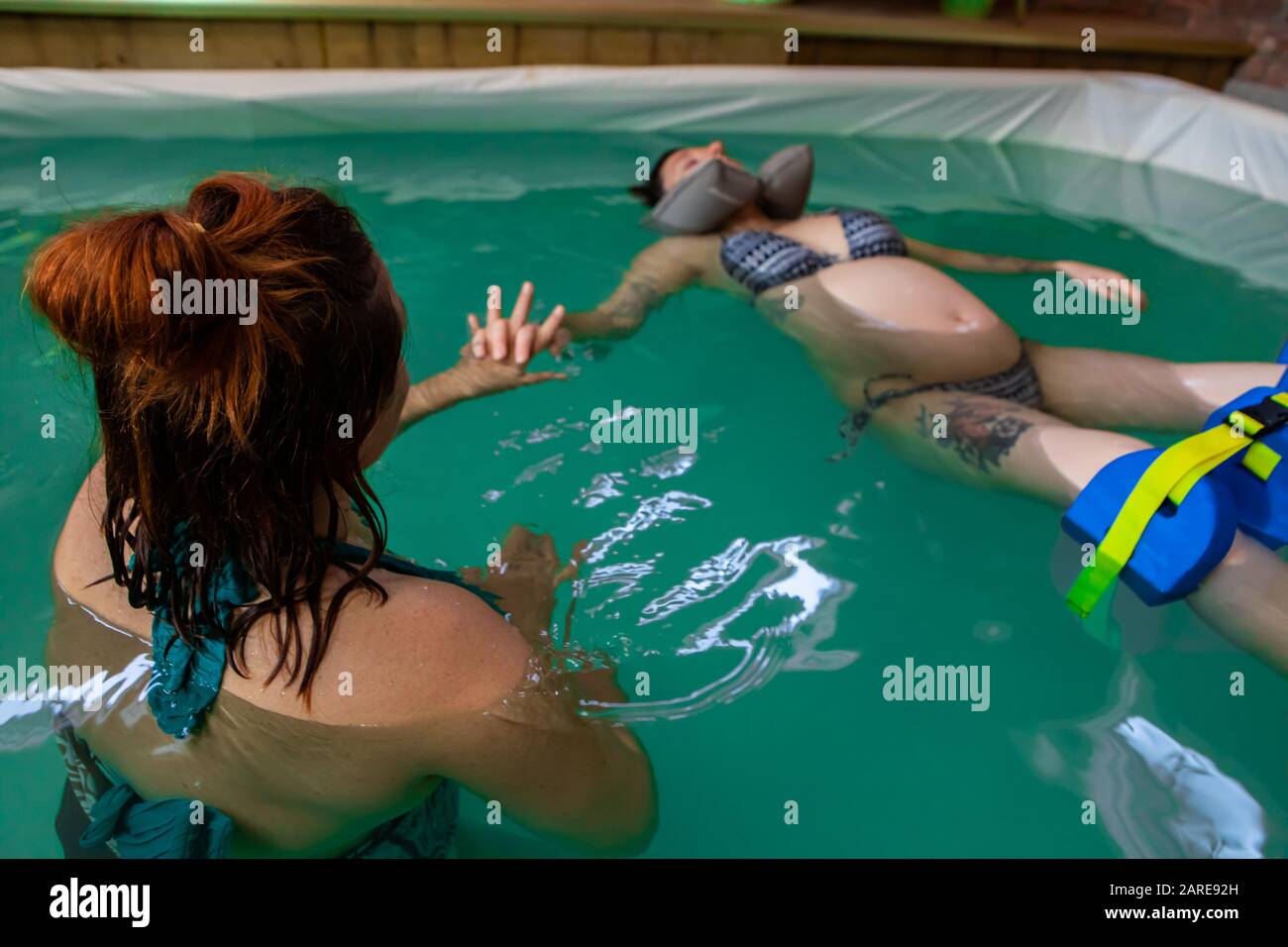 Femme enceinte détendue au maillot bleu reposant sur le dos avec oreiller à col en caoutchouc dans la petite piscine tout en recevant un bain bouillonnant Banque D'Images Femme enceinte détendue au maillot bleu reposant sur le dos avec oreiller à col en caoutchouc dans la petite piscine tout en recevant un bain bouillonnant Banque D'Images