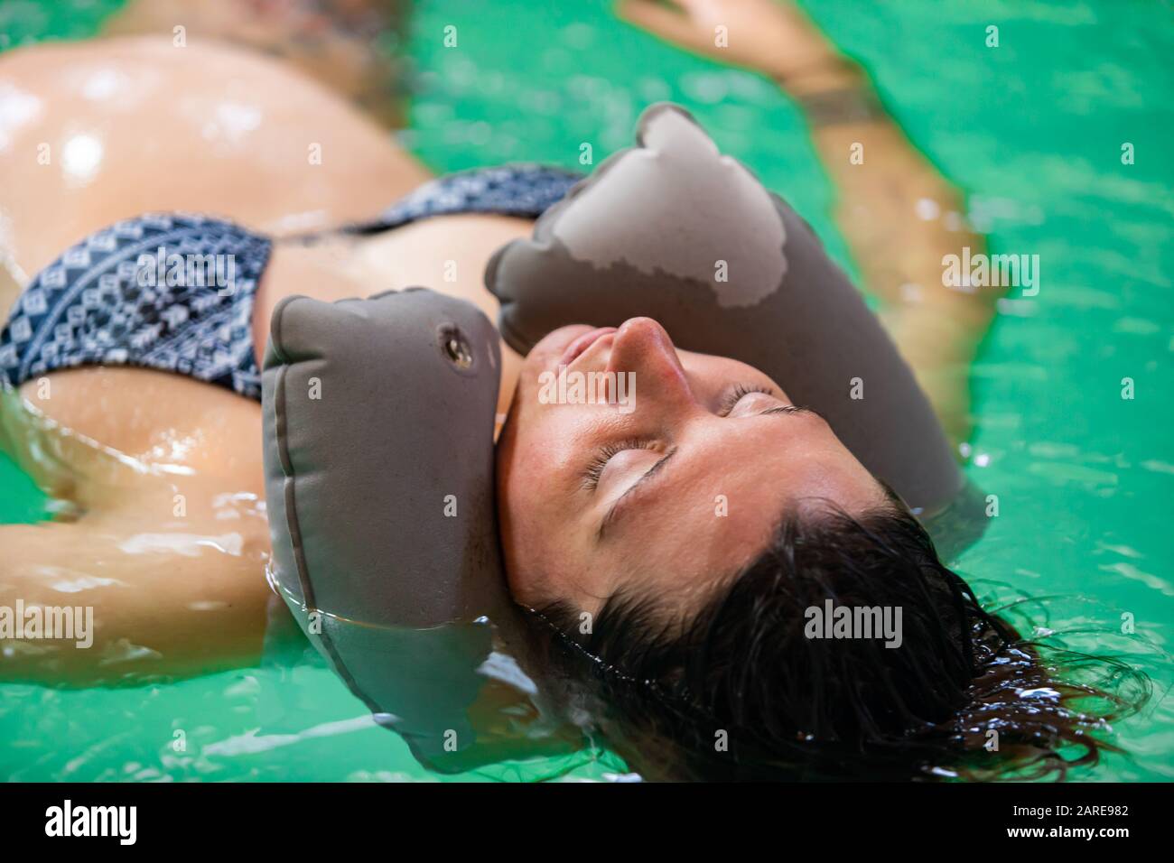 Gros plan de la femme enceinte avec oreiller à col en caoutchouc flottant  sur l'eau avec des yeux fermés tout en recevant un bain à remous dans la  piscine Photo Stock -