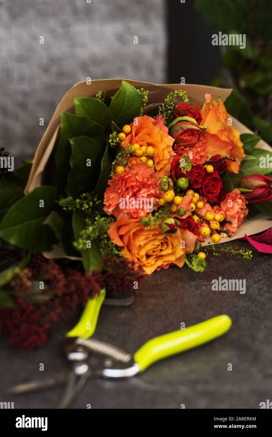 Bouquet de fleurs rouge et orange sur surface en pierre. Un bouquet assemblé de fleurs dans un emballage en papier à côté de ciseaux ou d'un pruner de fleuriste. Banque D'Images