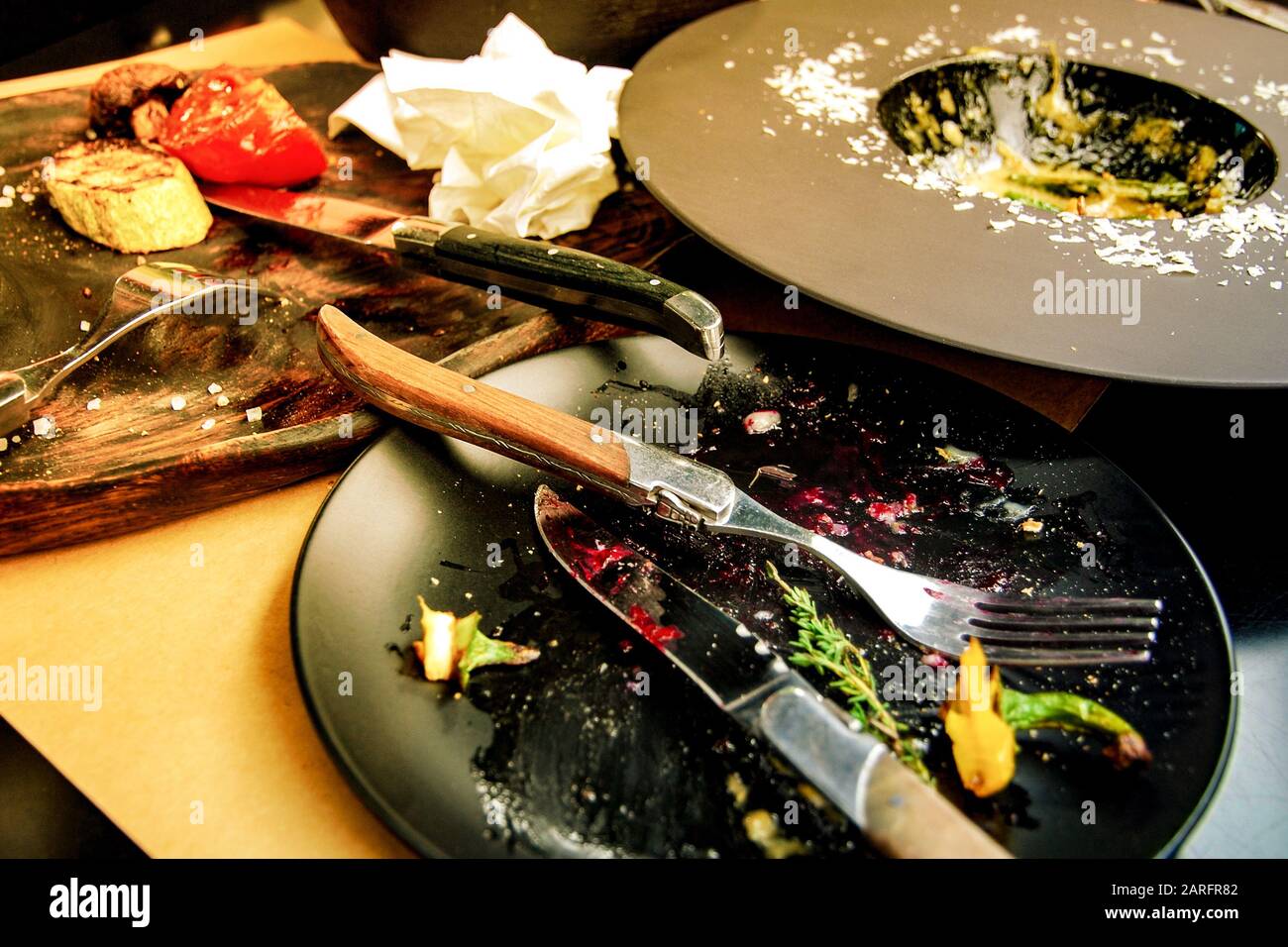 Table au restaurant avec des restes de nourriture sur des assiettes noires Banque D'Images