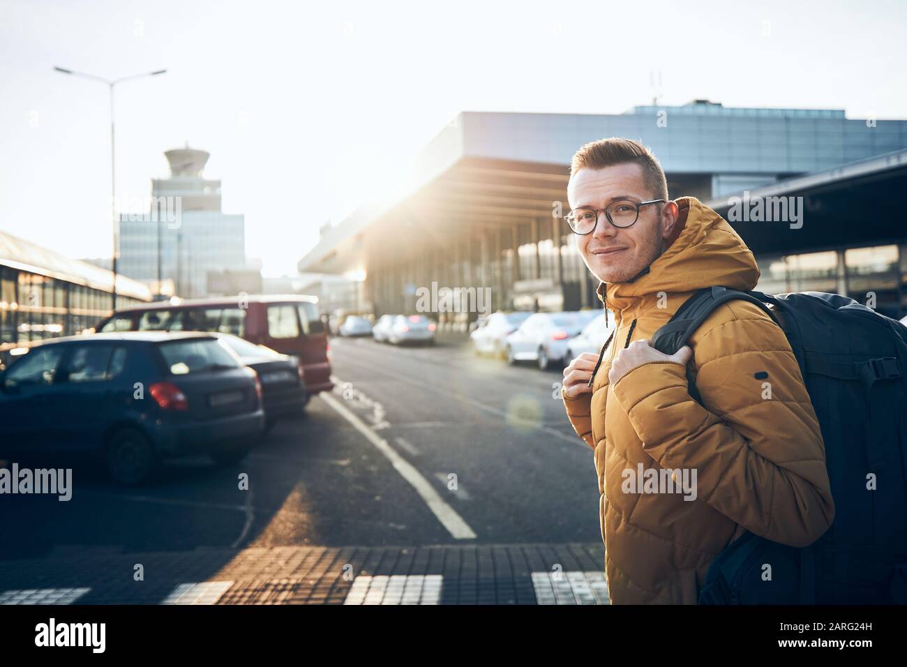 Jeune homme souriant avec sac à dos sur le parking de l'aéroport aganiste terminal bâtiment au coucher du soleil. Banque D'Images