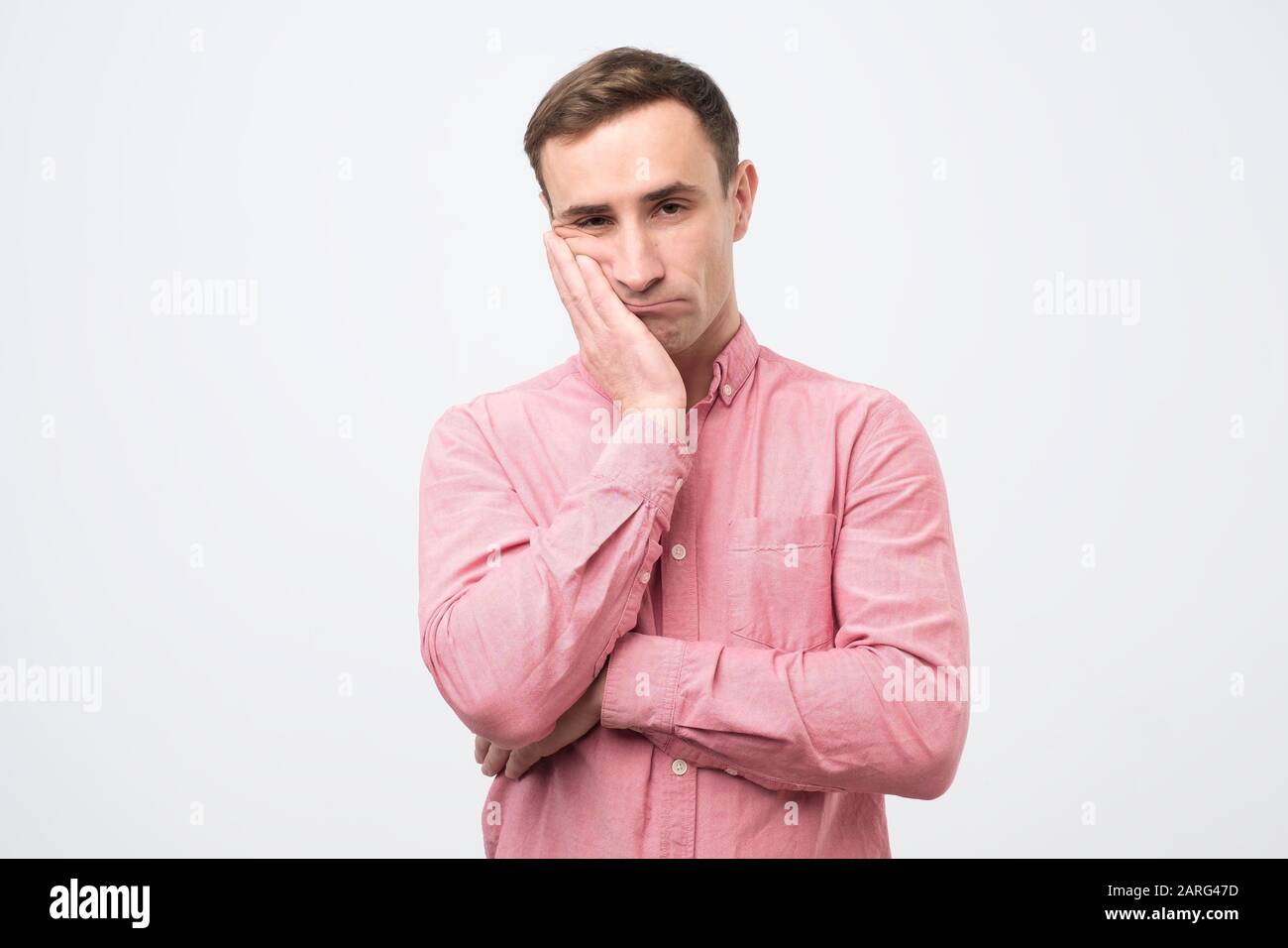 Homme italien adulte très ennuyé dans une chemise rose tenant la main sur  la joue à l'air fatigué et malade, sur fond blanc. Le père assiste à la  journée des parents à