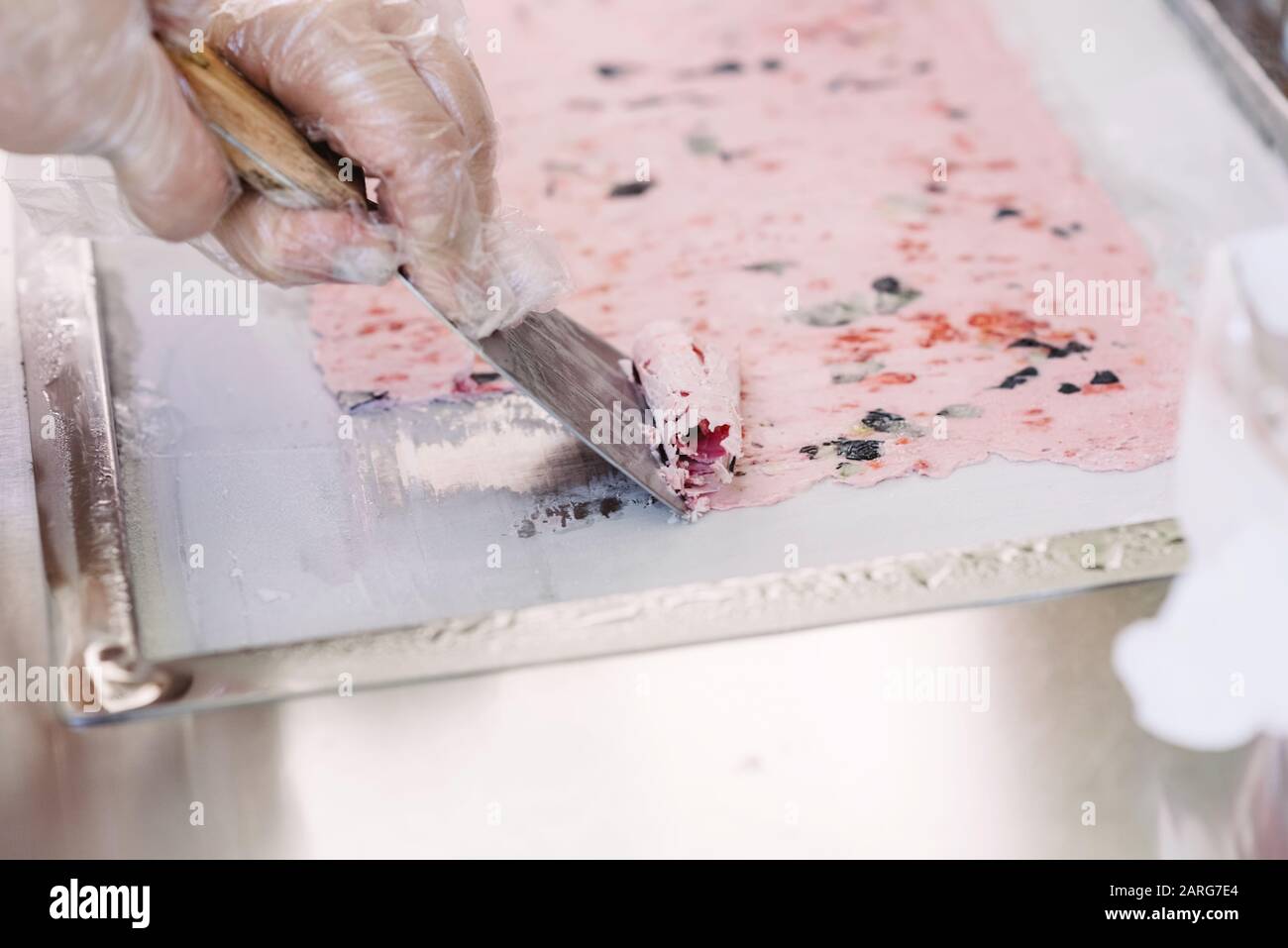 Création de glace sur l'équipement de réfrigération. Le cuisinier tord une fine feuille de crème glacée dans un rouleau. Mise au point sélective Banque D'Images