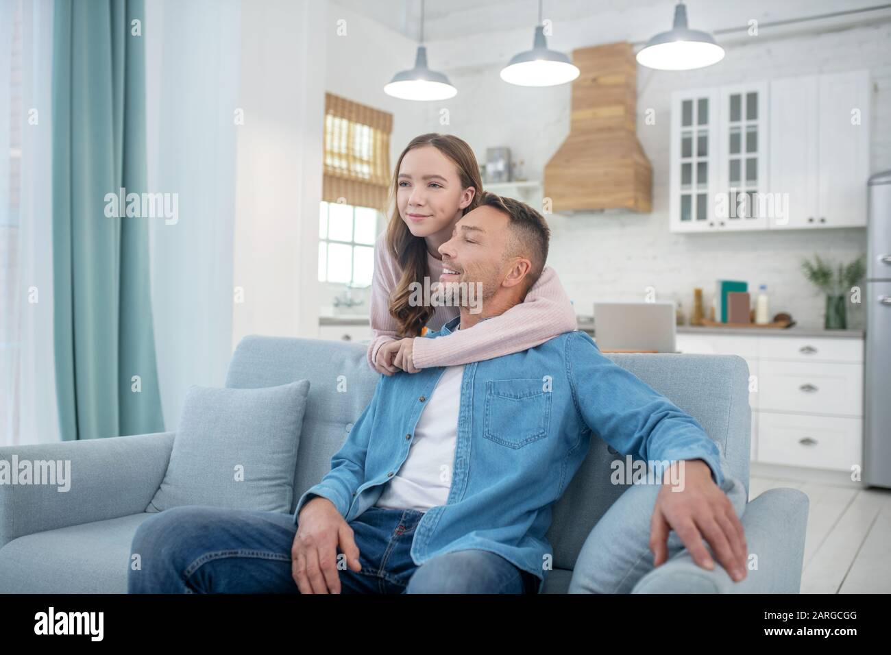 Fille embrassant son père, qui est assis sur le canapé. Banque D'Images
