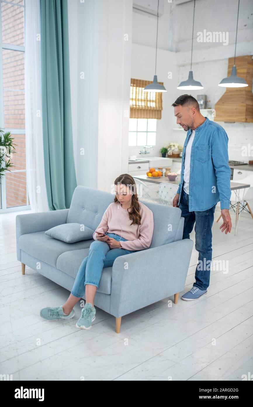 Fille avec casque assis sur le canapé et père debout à proximité. Banque D'Images