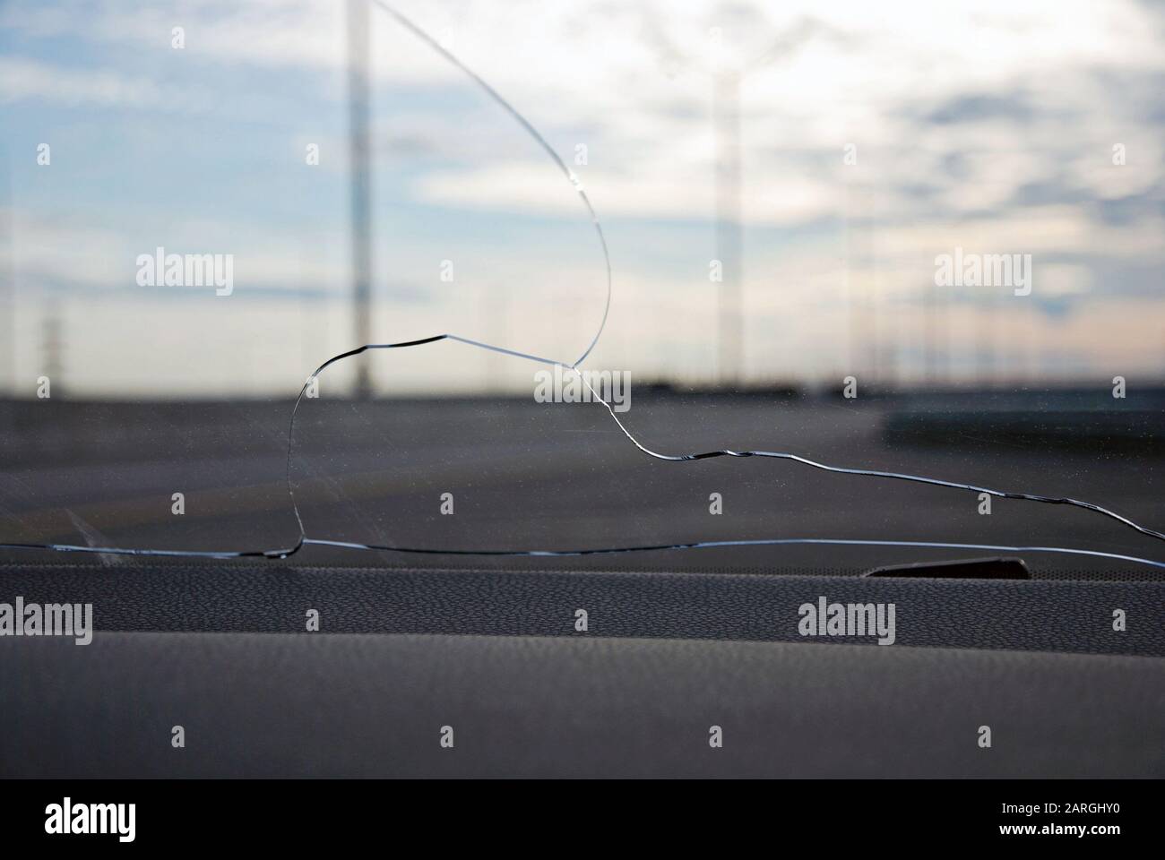 Fissures sur la vitre du pare-brise de la voiture frappées par la pierre éjectée sous les roues d'une autre voiture. Vue de l'intérieur contre l'autoroute vide Banque D'Images