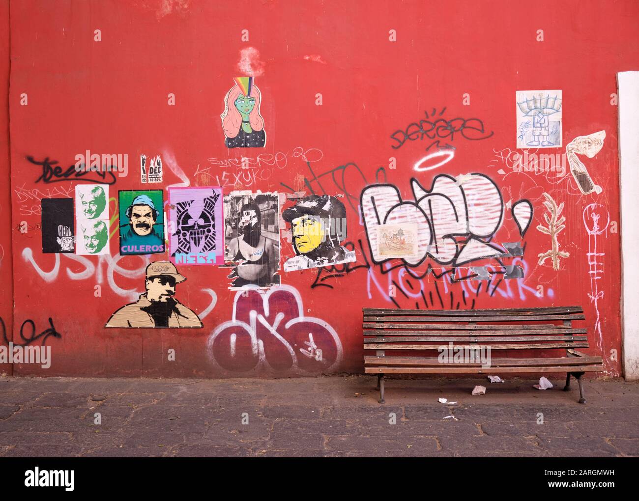 Mur rouge dans la vieille ville coloniale de Puebla recouvert de divers affiches d'art décalque et graffitis avec un banc de bois vide Banque D'Images