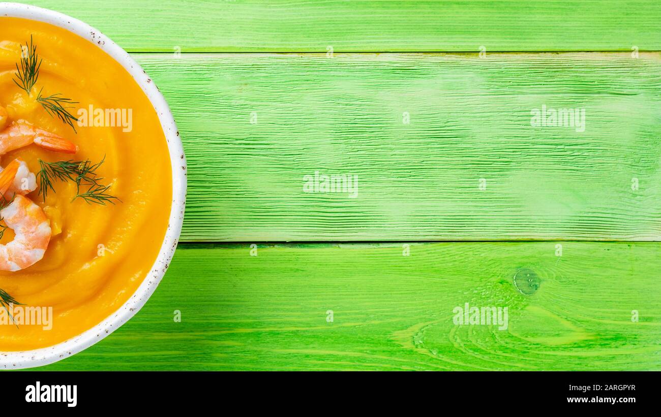 Délicieuse soupe de crème de citrouille jaune aux crevettes sur une table en bois vert vif, vue sur le dessus, espace de copie, bannière de format long Banque D'Images