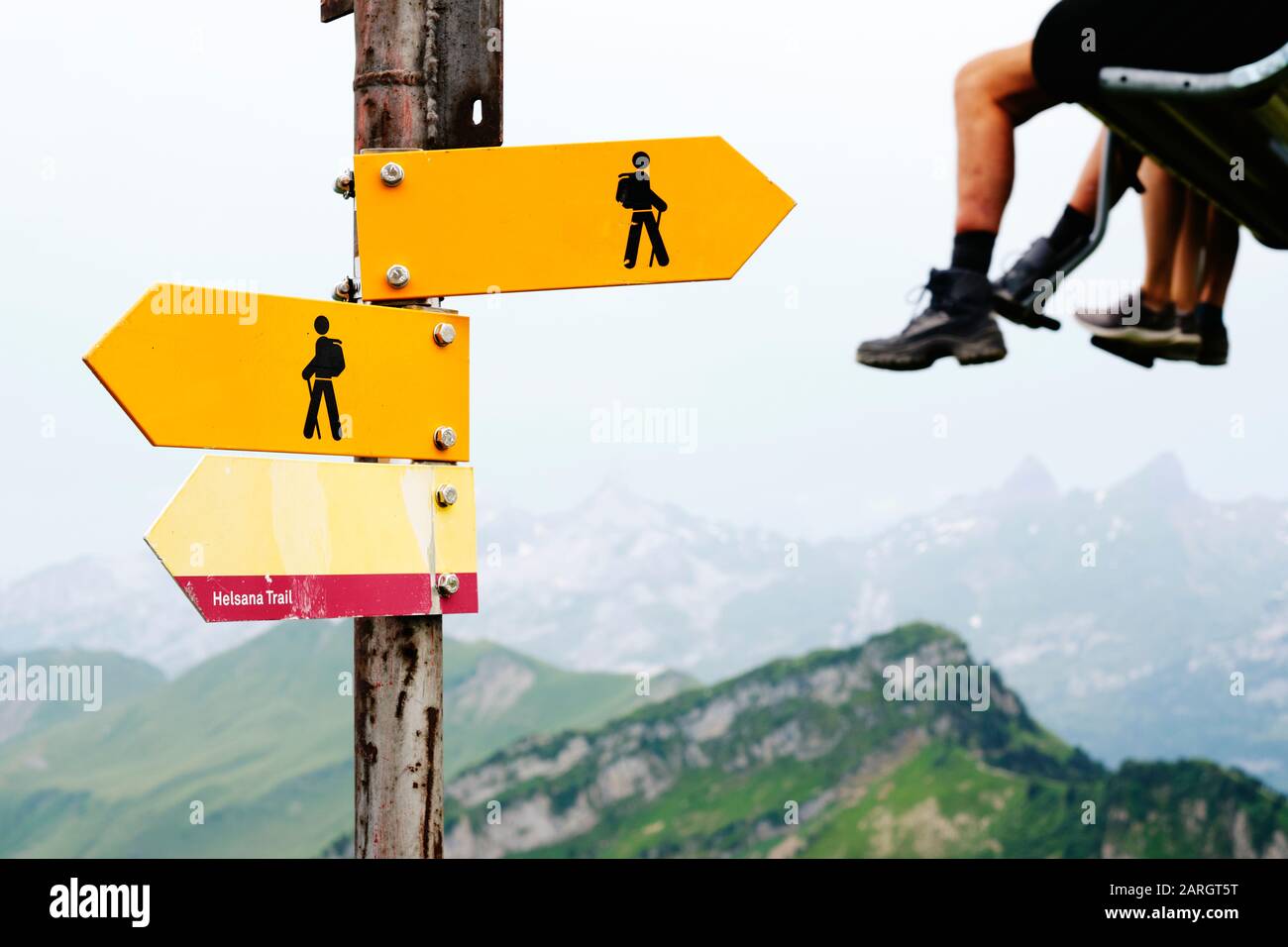 Un sentier de randonnée pédestre des alpes d'été signpost dans un paysage de montagne avec des randonneurs jambes sur un télésiège en arrière-plan - hors tourisme vacances à pied Banque D'Images