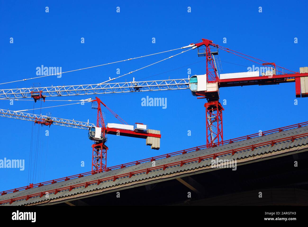 Deux grues de construction rouges et blanches sur un toit diagonal contre le ciel bleu Banque D'Images
