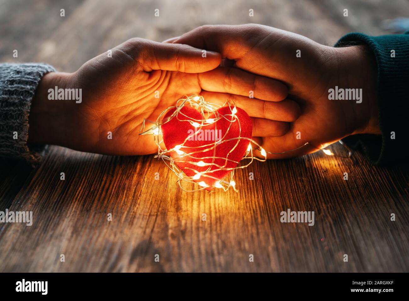 Deux mains tenant une forme de coeur rouge couverte de lumières LED sur fond de bois et de bokeh lumières. Saint Valentin et concept romantique Banque D'Images