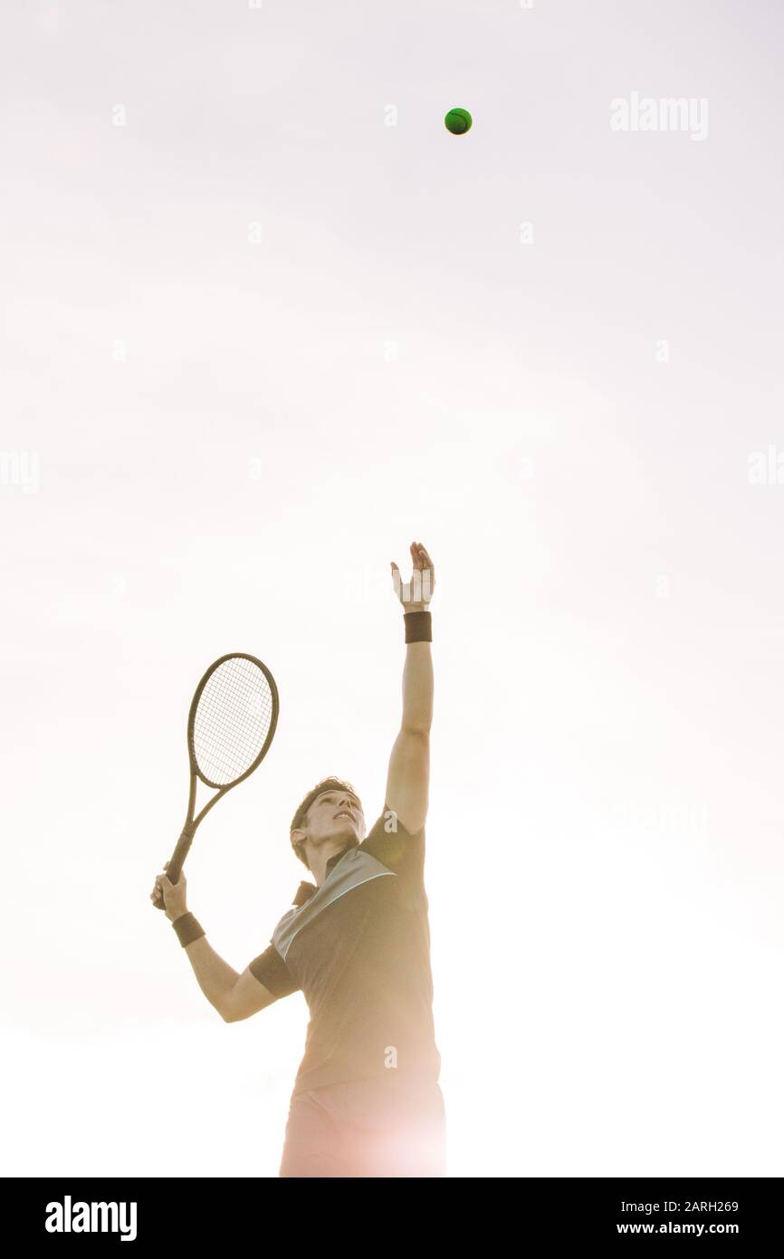 Un joueur de tennis masculin qui lance une balle pour le servir une journée ensoleillée. Le joueur de tennis sert une balle dans un match. Banque D'Images