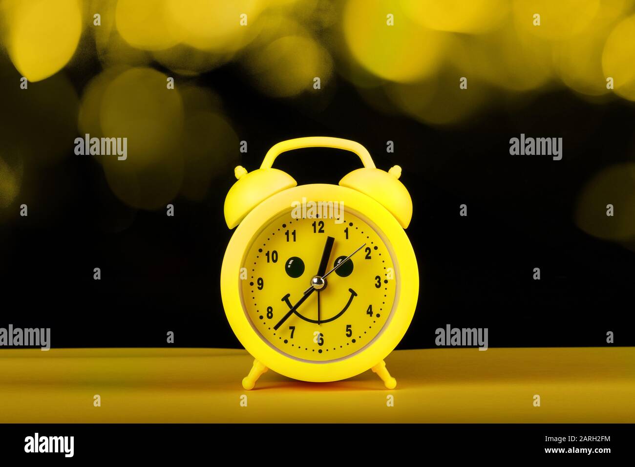 Réveil jaune avec smililng face sur la table et bokeh lumières sur fond noir. Concept de gestion du temps Banque D'Images