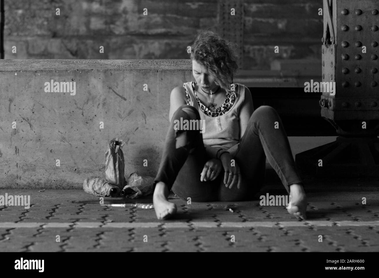 une femme désespérée punk sous un pont avec des bouteilles d'alcool et d'autres drogues autour d'elle Banque D'Images