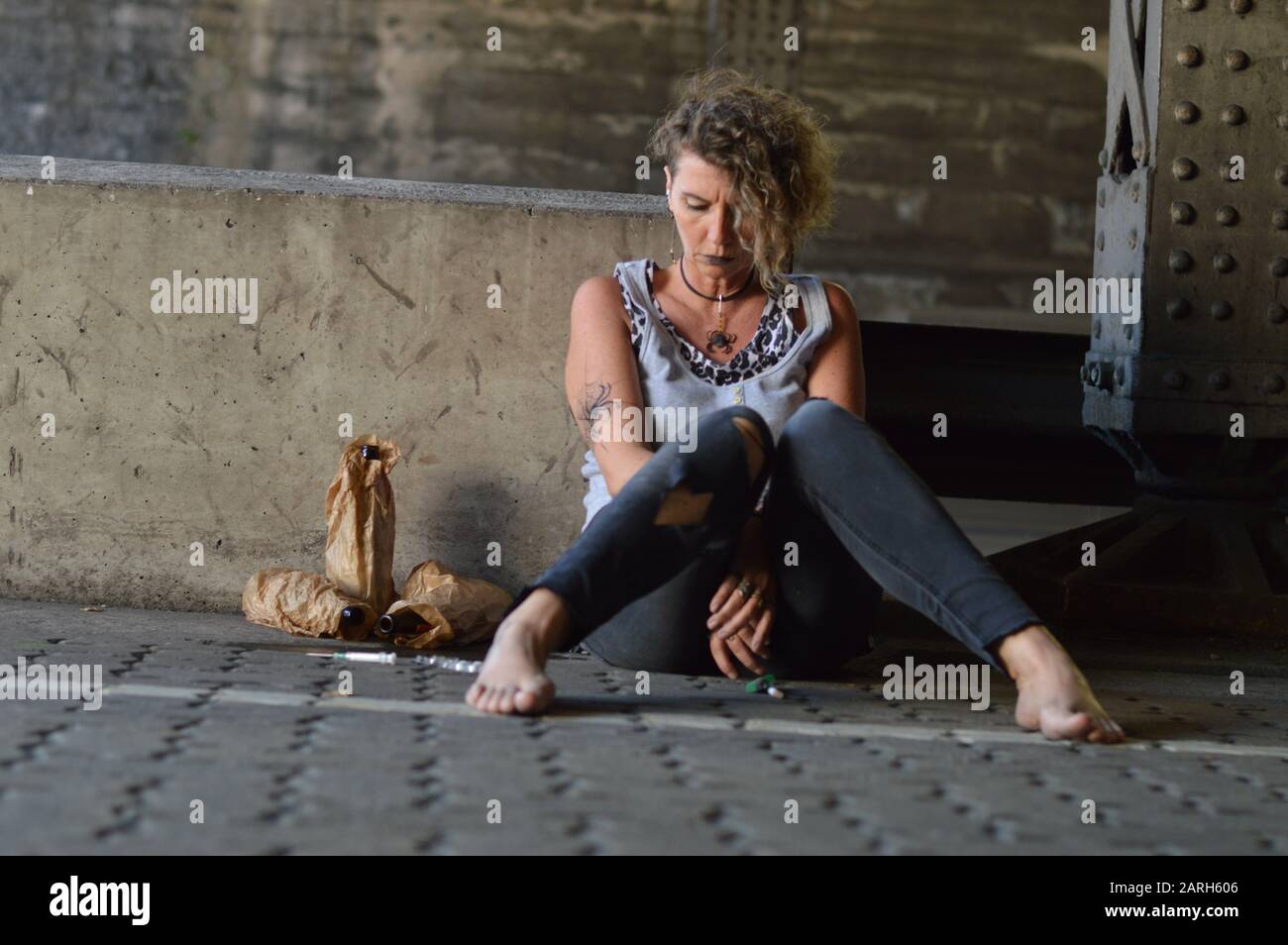 une femme désespérée punk sous un pont avec des bouteilles d'alcool et d'autres drogues autour d'elle Banque D'Images