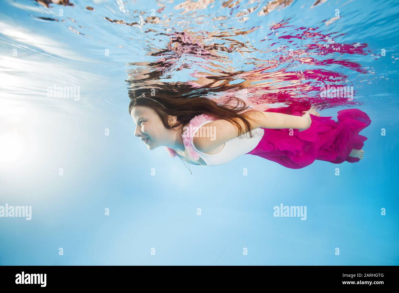 Drôle de fille dans des robes roses portant des poses sous l'eau. La jeune belle fille pose sous l'eau dans la piscine. Banque D'Images