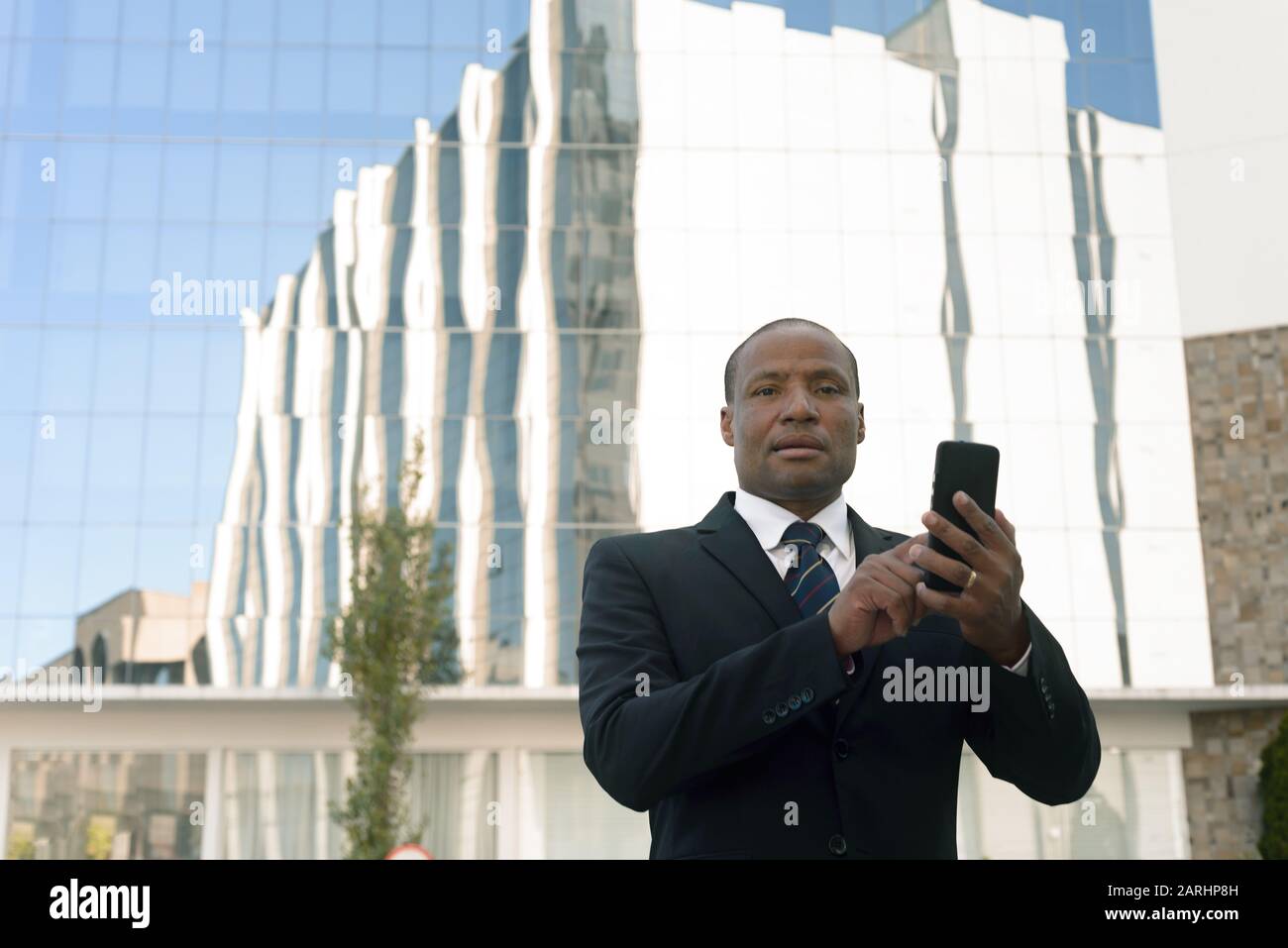 Homme d'affaires noir dans un costume regardant avec succès un smartphone en milieu urbain Banque D'Images
