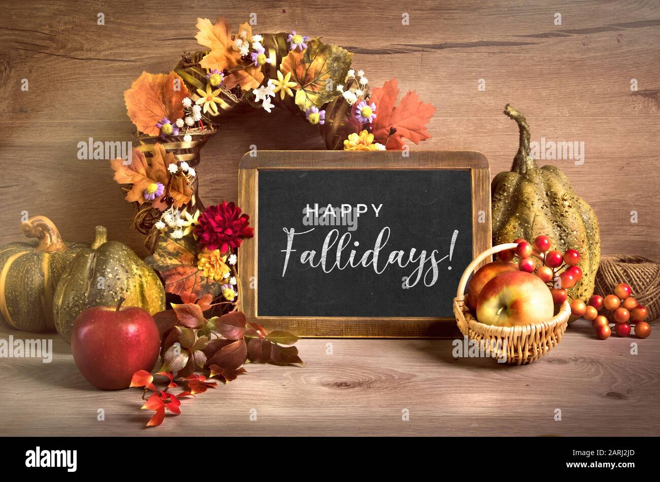 Arrangement d'automne avec couronne et lettrage 'Happy Fallidays' sur un tableau de craie. Panier de pommes et de baies, citrouilles décoratives, feuilles d'automne et Banque D'Images