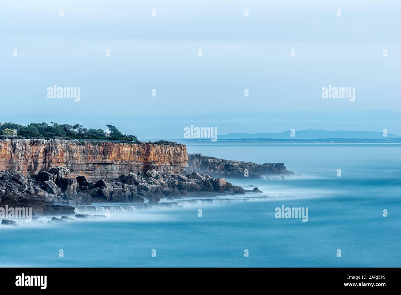 Les falaises et l'océan Atlantique par le site touristique Boca do Inferno à Cascais Portugal en après-midi soleil avec des mers lisses qui s'écrasent sur les rochers avec une longue exposition Banque D'Images