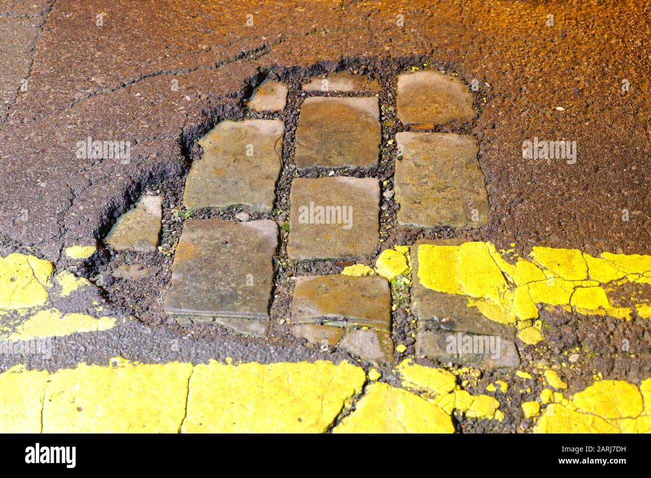 Une section cassée de la surface de la route du tarmac, révèle une ancienne route pavée de pierre victorienne à Leeds. Banque D'Images