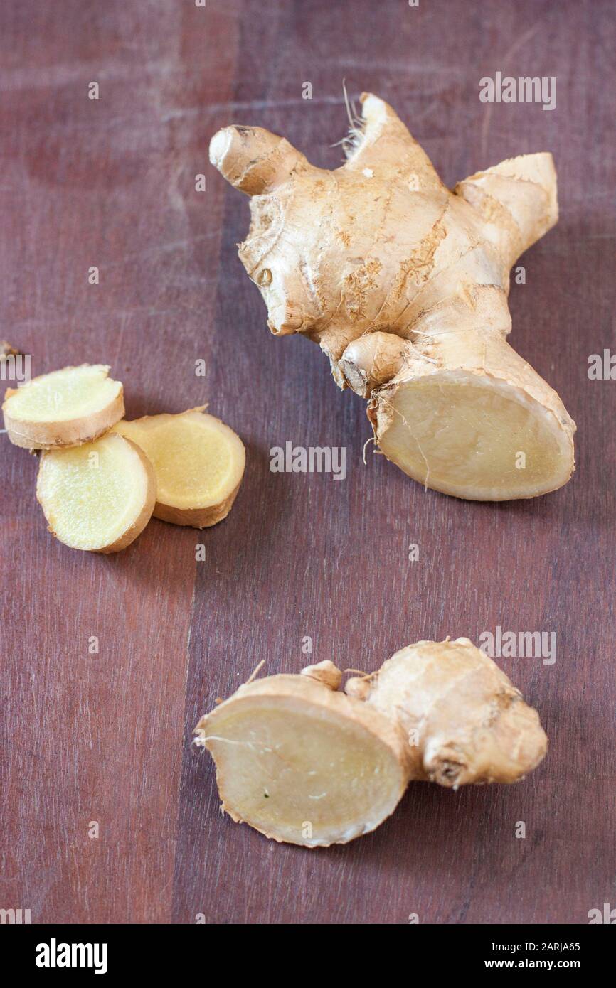 Racine de gingembre frais coupée en morceaux et en tranches sur fond de bois brun foncé Banque D'Images