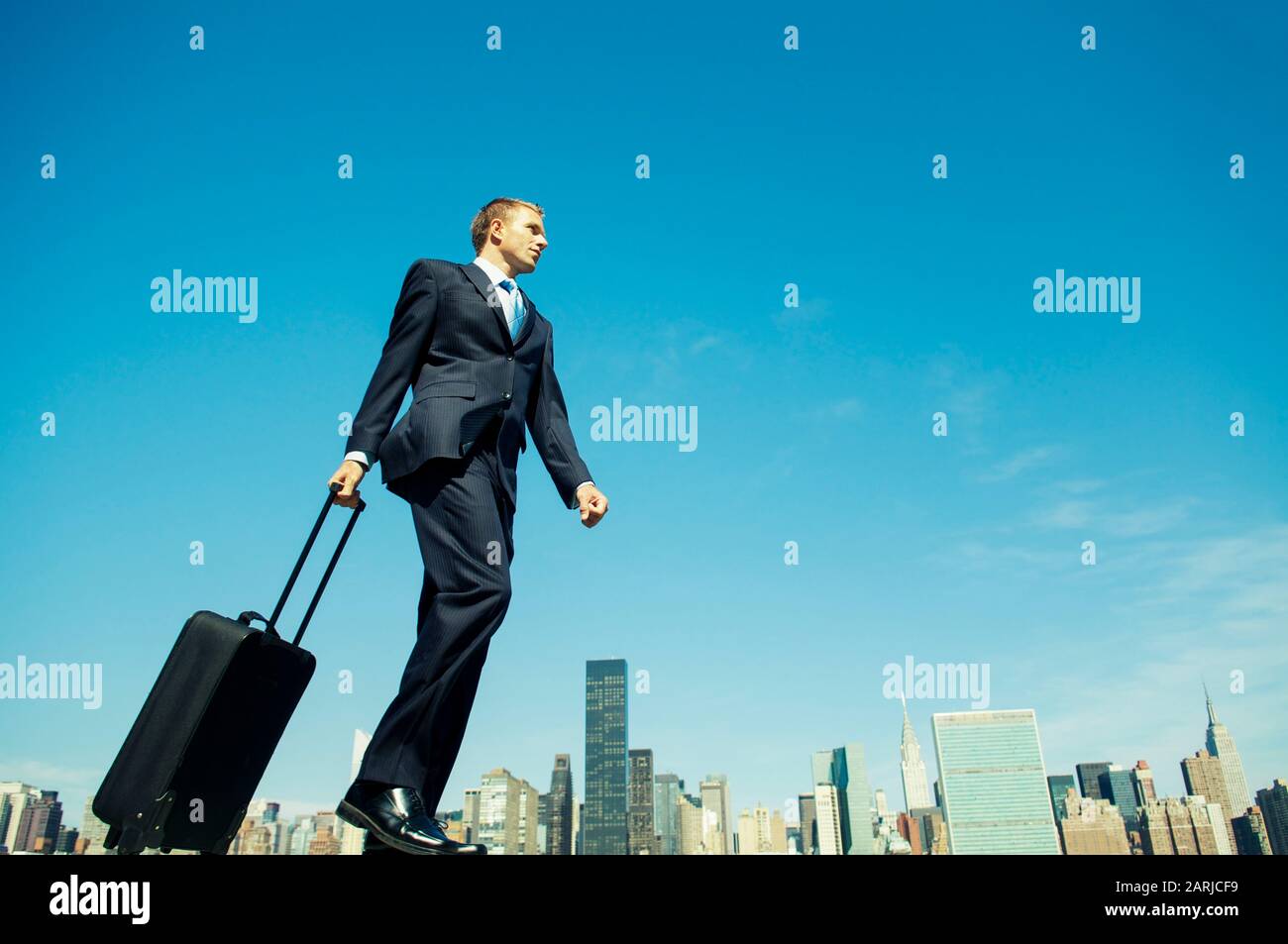 Un homme d'affaires itinérant géant qui marche avec sa valise à roulettes à  travers les gratte-ciel de la ville sous le ciel bleu ensoleillé Photo  Stock - Alamy