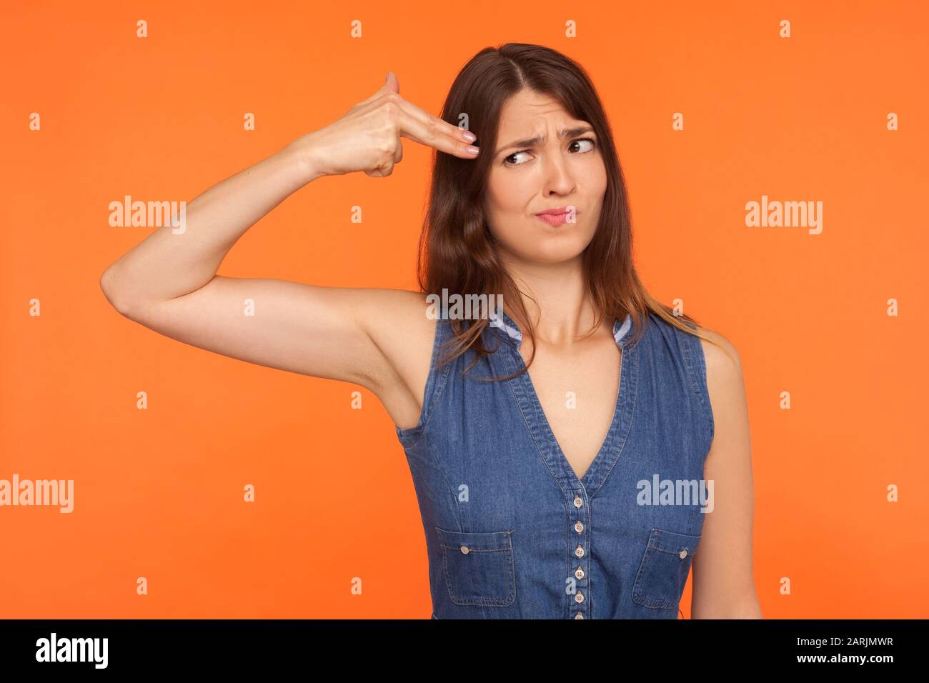 Une femme désespérée brunette en robe denim qui avait peur d'un pistolet à doigts pointé vers la tête, se tuant avec un geste suicide, effrayée, fatiguée de la vie. Banque D'Images