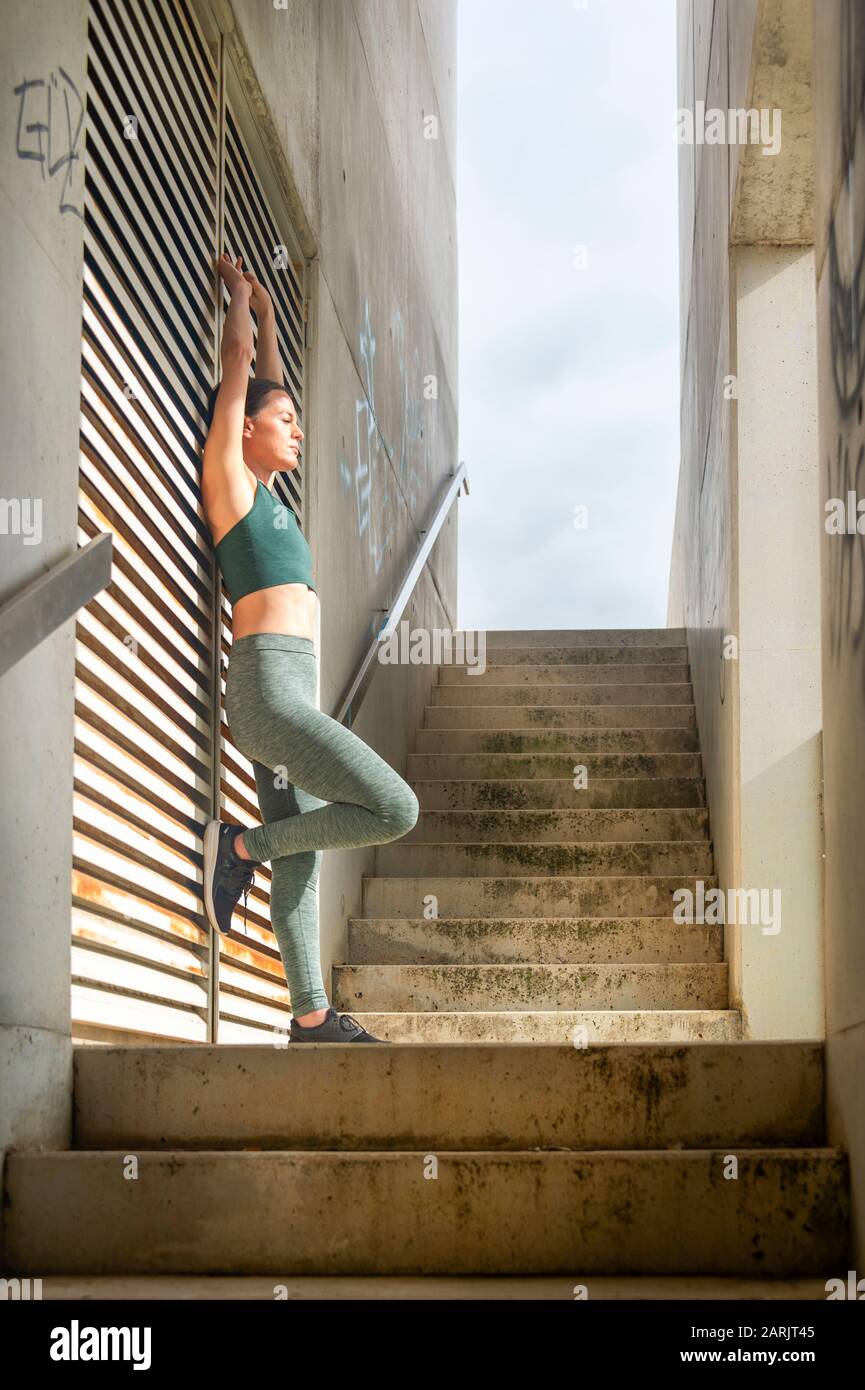 Une femme sportive se reposant après un exercice dans un cadre urbain moderne, bras extensible. Banque D'Images