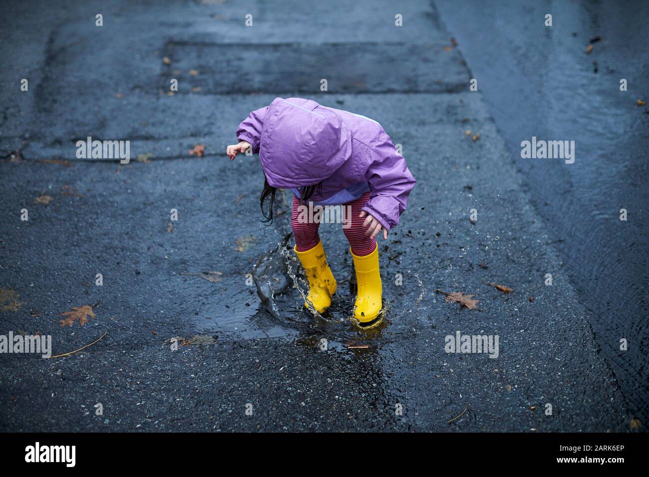 Une petite fille qui s'amuse à barboter dans les flaques par temps pluvieux. Banque D'Images