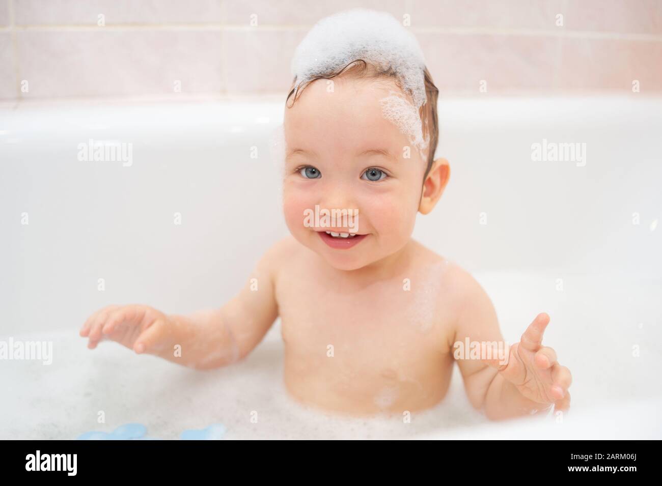 Une petite fille avec de la mousse sur sa tête sourit dans la salle de bains. Jolie fille de bébé est heureuse dans la salle de bains. Adorable petit portrait de bébé. Soins De La Peau. Santé c Banque D'Images