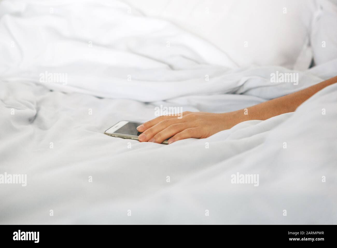 La main de gros plan maintient le téléphone dans le lit. La fille s'est endormie avec un téléphone dans sa main et elle est accro. Ou une personne atteint pour qu'un téléphone mobile désactive l'alarme. Banque D'Images
