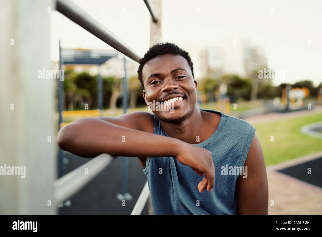Portrait souriant d'un jeune homme sportif africain américain se penchant sur le bar du parc public en regardant un appareil photo avec un grand sourire Banque D'Images